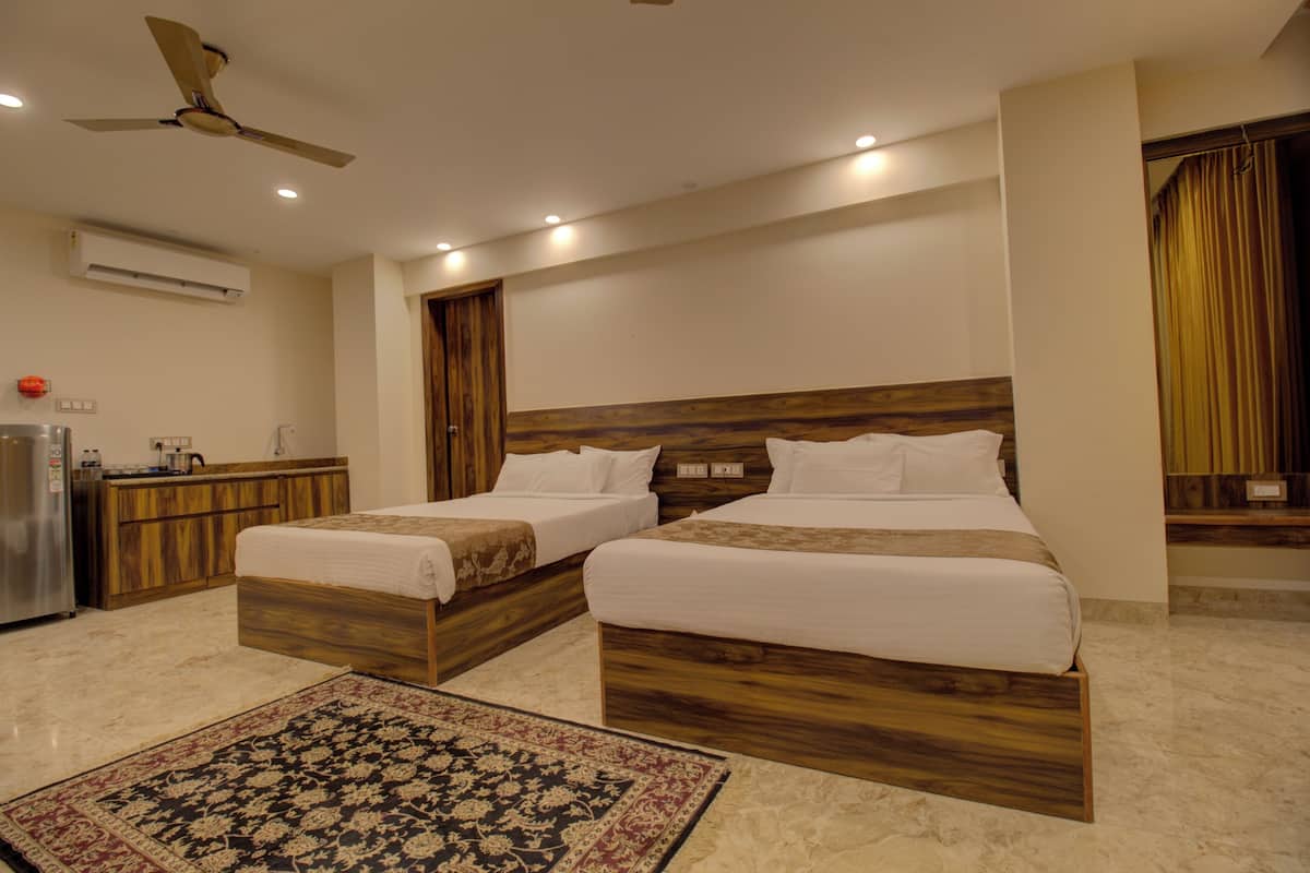 Une chambre d’hôtel avec deux lits, une tête de lit en bois, un ventilateur de plafond, un appareil de climatisation, une petite kitchenette et un tapis à motifs.