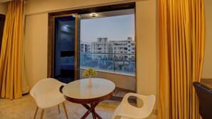 A hotel room with a balcony, a round table with a vase, and two chairs. - Greenstones Boutique Hotel (Nashik)