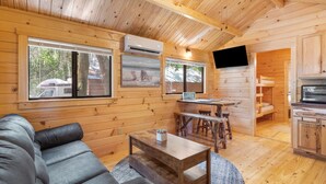 Ein gemütliches Blockhaus-Interieur mit Holzvertäfelung, einer Couch, einem Esstisch und einer Küchenzeile.