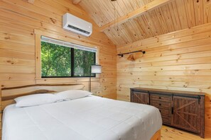 A wooden cabin bedroom with a bed, a window, and a cabinet.