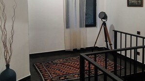 A room with a wooden ceiling, a window with curtains, a tripod, a framed picture on the wall, and a patterned rug on the floor. - Innwoods Hotel (Alaverdi)