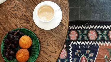 Una mesa redonda de madera con un plato de uvas y muffins, una taza de café y un vaso de té.