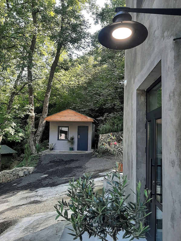 A modern building with a concrete exterior, a small wooden structure with a red roof in the background, and a street lamp. - Innwoods Hotel (Alaverdi)