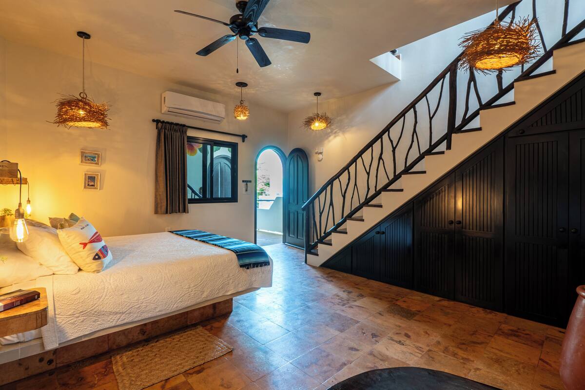 A bedroom with a bed, a wooden floor, a staircase, and a ceiling fan.