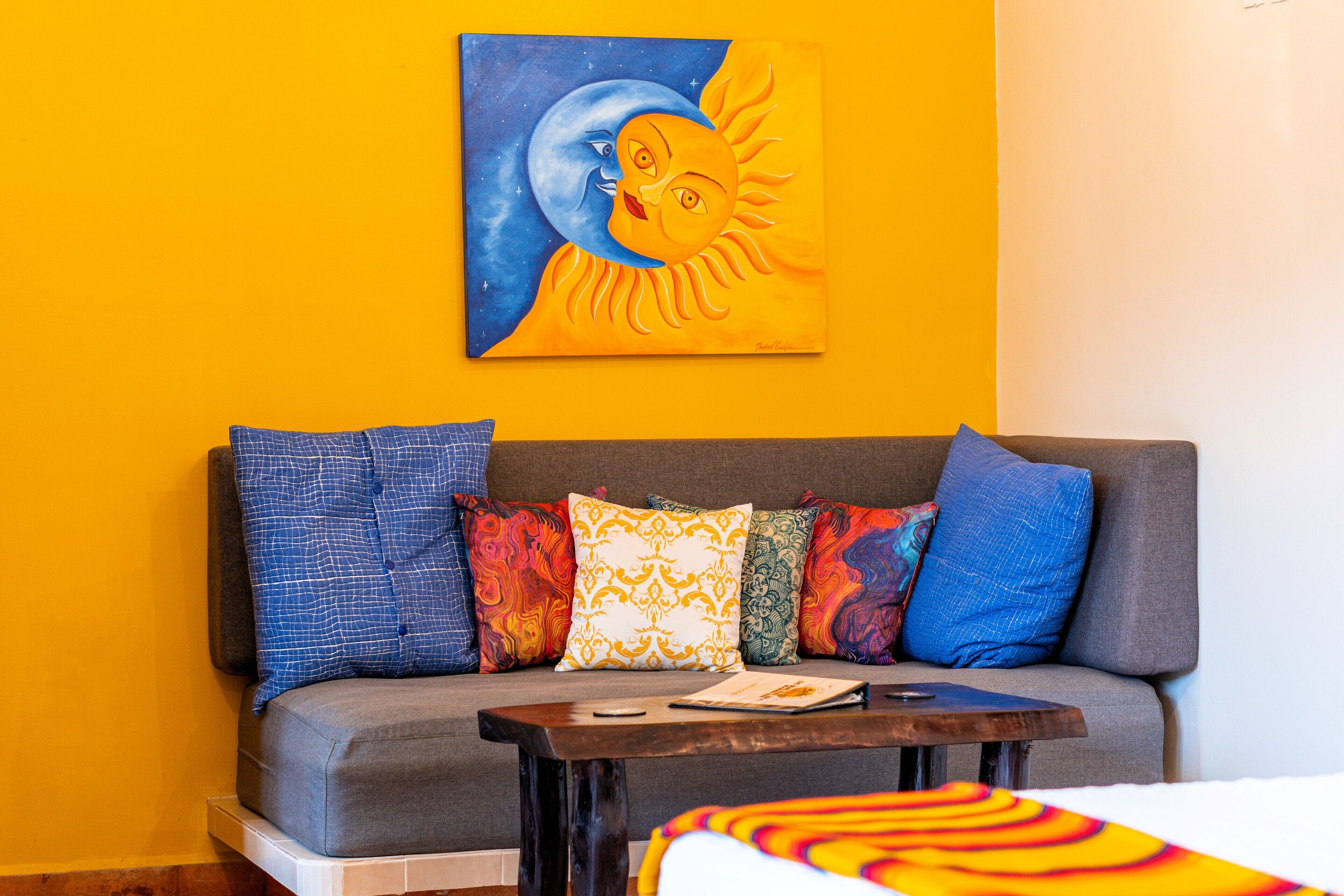 A room with a sofa against a yellow wall, a small table, and a painting of a sun and moon.