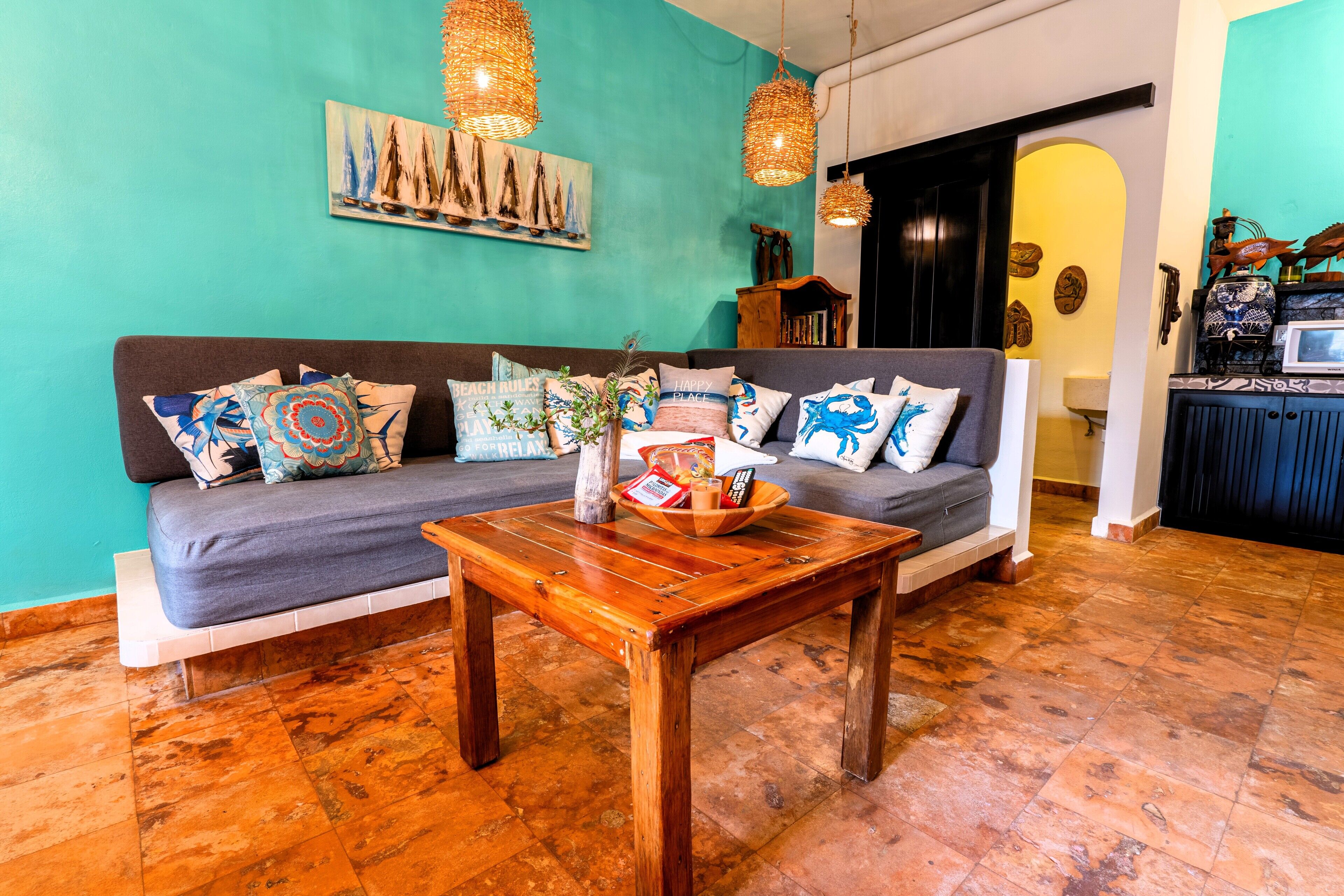 Un salon chaleureux avec un canapé gris, une table basse en bois et un mur de couleur turquoise orné d’un tableau représentant un voilier.