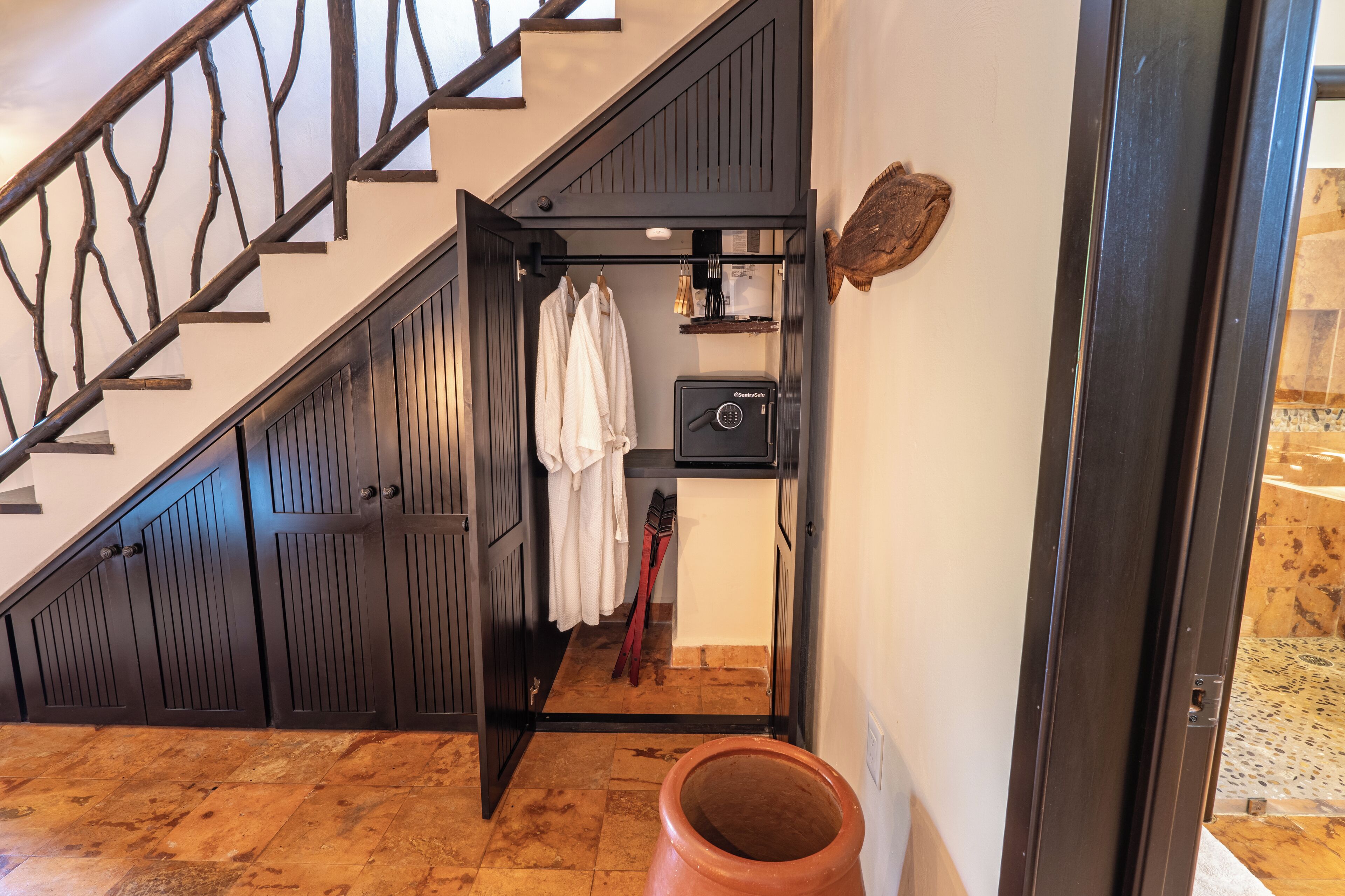 Una escalera con barandilla de madera, una puerta negra y una pared blanca decorada con un pez.