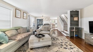 A living room with a sofa, ottoman, and a staircase leading to another level. - Charming 4-bed 2- Bath Home Close Proximity to Princeton Area and Sesame Place (Lawrence Township)