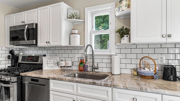 A modern kitchen with white cabinets, a stainless steel stove, a microwave, and a sink. - Charming 4-bed 2- Bath Home Close Proximity to Princeton Area and Sesame Place (Lawrence Township)