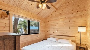 Una habitación de cabaña de madera con cama, ventana, ventilador de techo y mesita de noche.