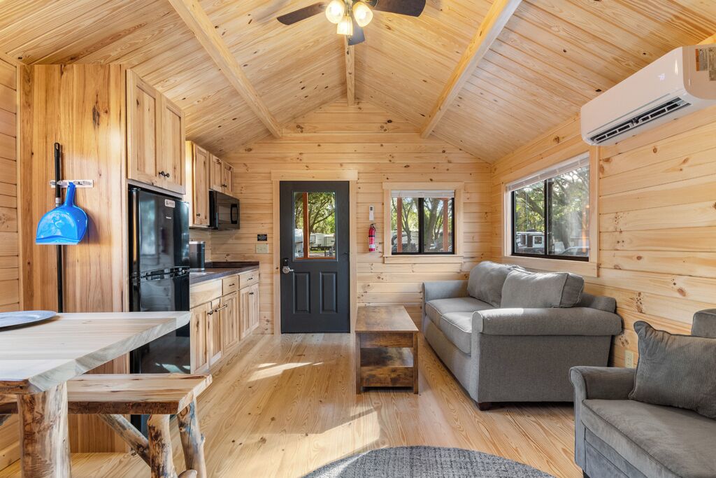 A wooden cabin interior with a kitchen, dining area, and living room.