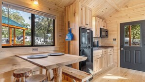 Cocina de cabaña de madera con una ventana grande, una mesa de comedor con taburetes y un refrigerador.