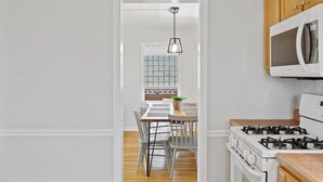 A modern kitchen with white cabinets, a gas stove, a microwave, and a dining area with a table and chairs. - Spaciuos House in Wexford (Wexford)