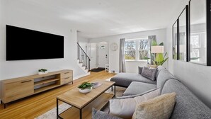 A modern living room with a flat-screen TV, wooden coffee table, grey sofa, and a staircase leading to another room. - Spaciuos House in Wexford (Wexford)