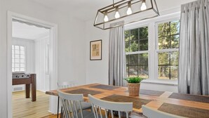 A dining area with a wooden table, white chairs, and a hanging light fixture. - Spaciuos House in Wexford (Wexford)