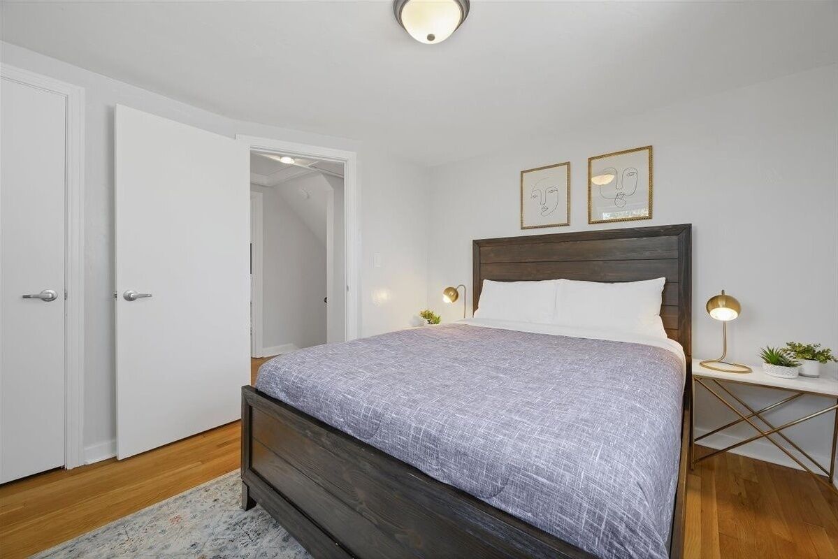 Une chambre à coucher avec un lit en bois, des murs blancs, une porte blanche et deux tables de chevet avec des lampes.
