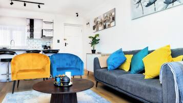 A modern living room with a grey sofa, blue and yellow cushions, a round coffee table, and two armchairs.