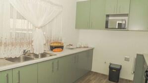 Una cocina con armarios verdes, un microondas, un lavabo y un cubo de basura.