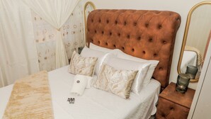 Una cama bien hecha con un cabecero capitonado, una mesita de noche con una lámpara y un espejo en la pared.