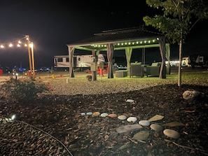 A covered outdoor seating area with a gazebo, a grill, and a row of chairs. - Tiny home mtn retreat-covered outdoor patio, firepit, pool, fishing, basketball (Morganton)