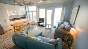 Ein modernes Wohnzimmer mit einer Couch, einem Couchtisch und einem Fernseher. Es gibt einen Essbereich mit Tisch und Stühlen.