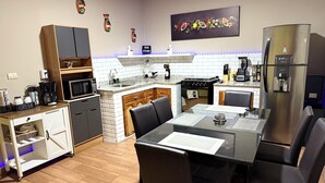 A modern kitchen with a dining area, featuring a refrigerator, stove, microwave, and coffee station.