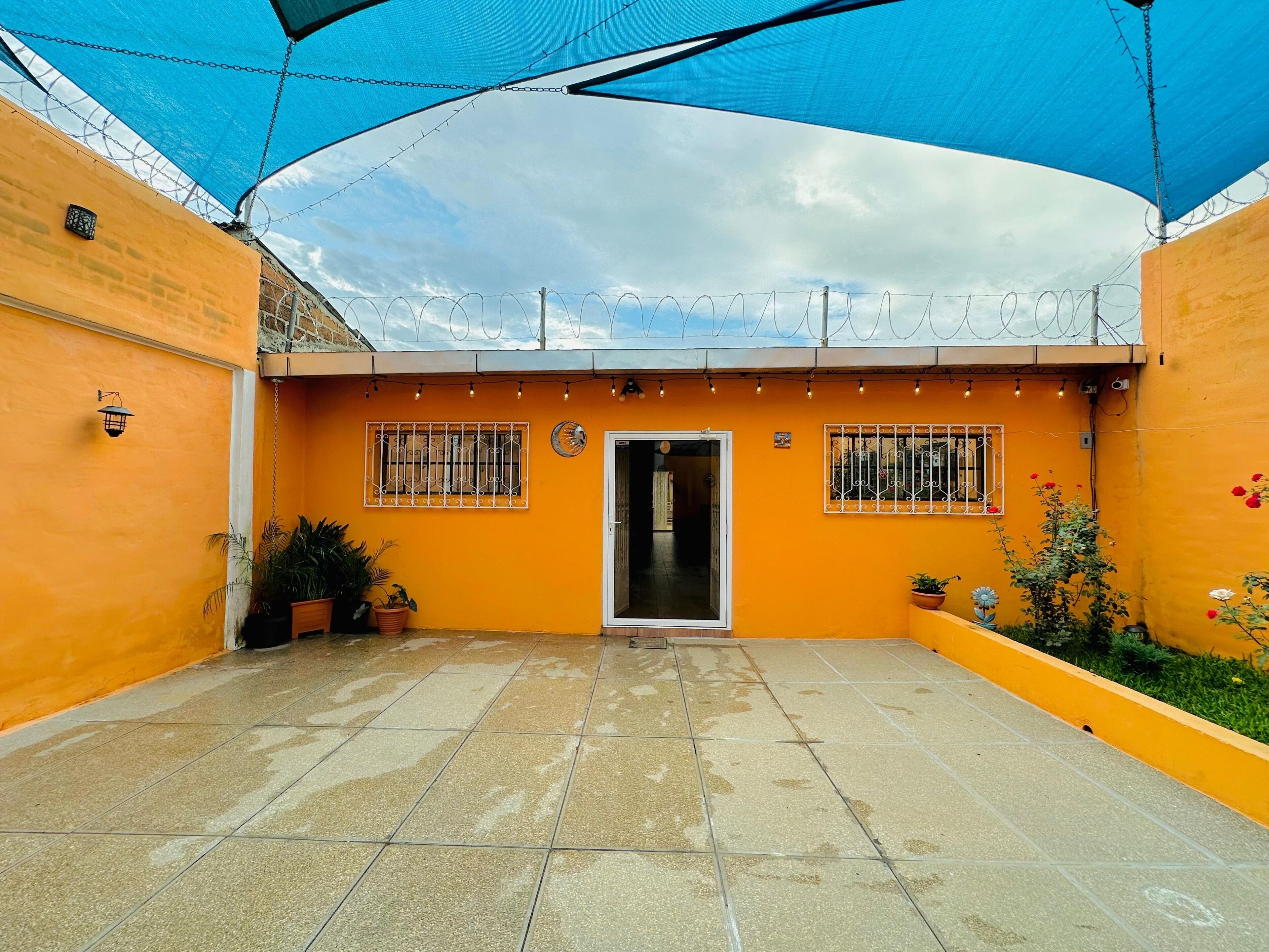 Un patio con un toldo azul, paredes anaranjadas y piso de baldosas.
