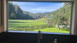 Une cuisine dotée d’une grande fenêtre donnant sur un champ verdoyant et bordée d’une clôture en bois.