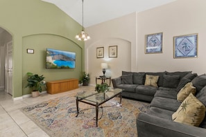 A living room with a sofa, a glass coffee table, a TV, and framed artwork on the wall.