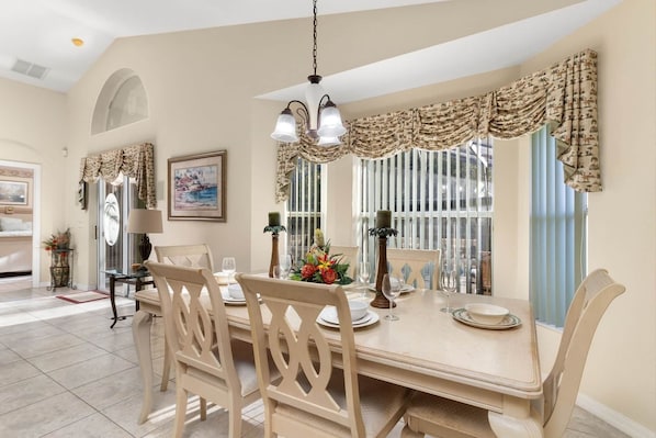A dining area with a table set for four, surrounded by chairs, with a chandelier above.