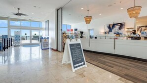 A general store with a clean, modern interior, featuring a reception desk, a chalkboard sign, and a view of the beach through large windows.
