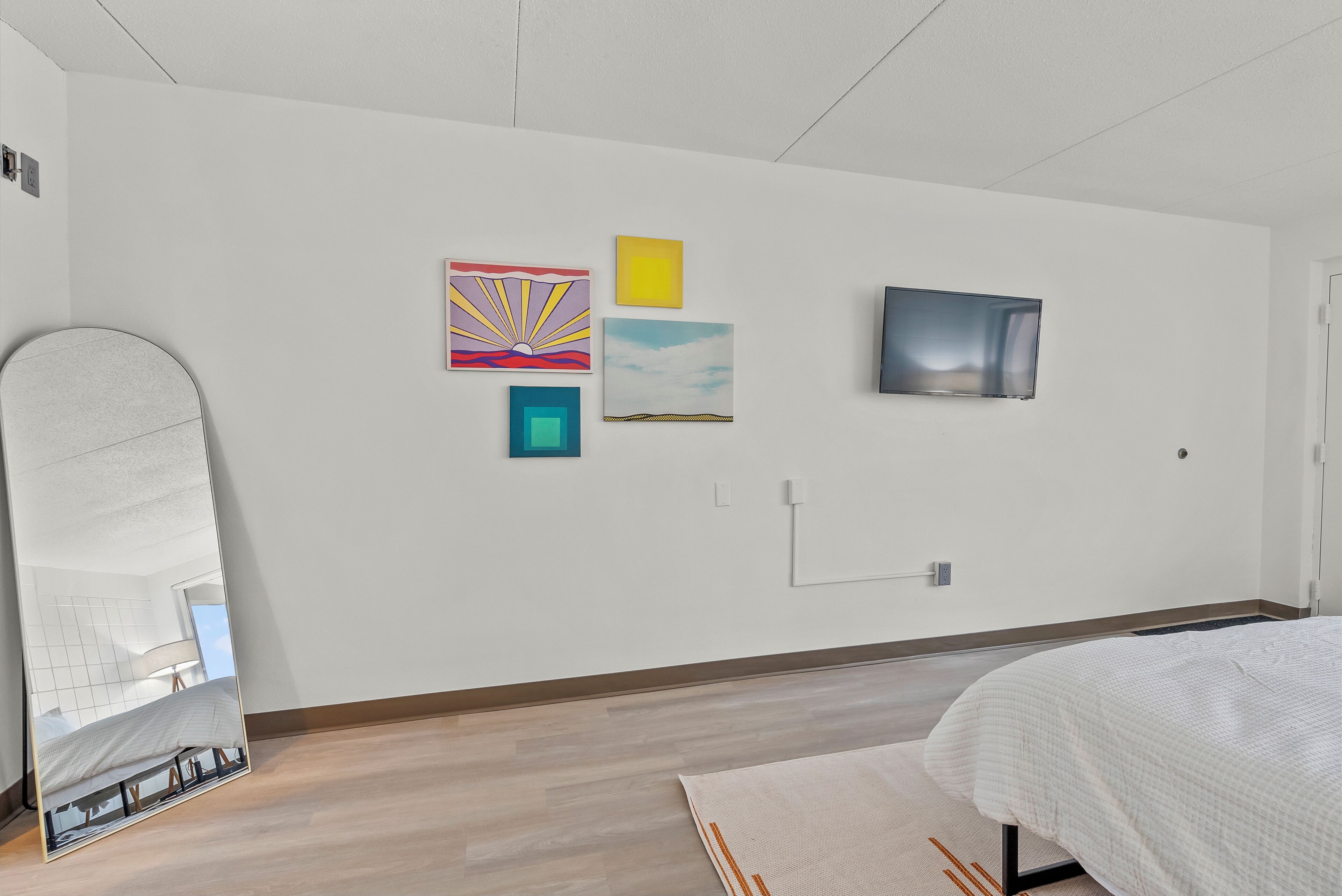 Un dormitorio moderno con una cama, un espejo grande y obras de arte en la pared.