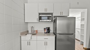 A compact kitchen with white cabinets, a stainless steel refrigerator, a microwave, and a coffee maker. - Stay Downtown, Free Gated Parking, Renovated Studio! 512 (Cedar Falls)