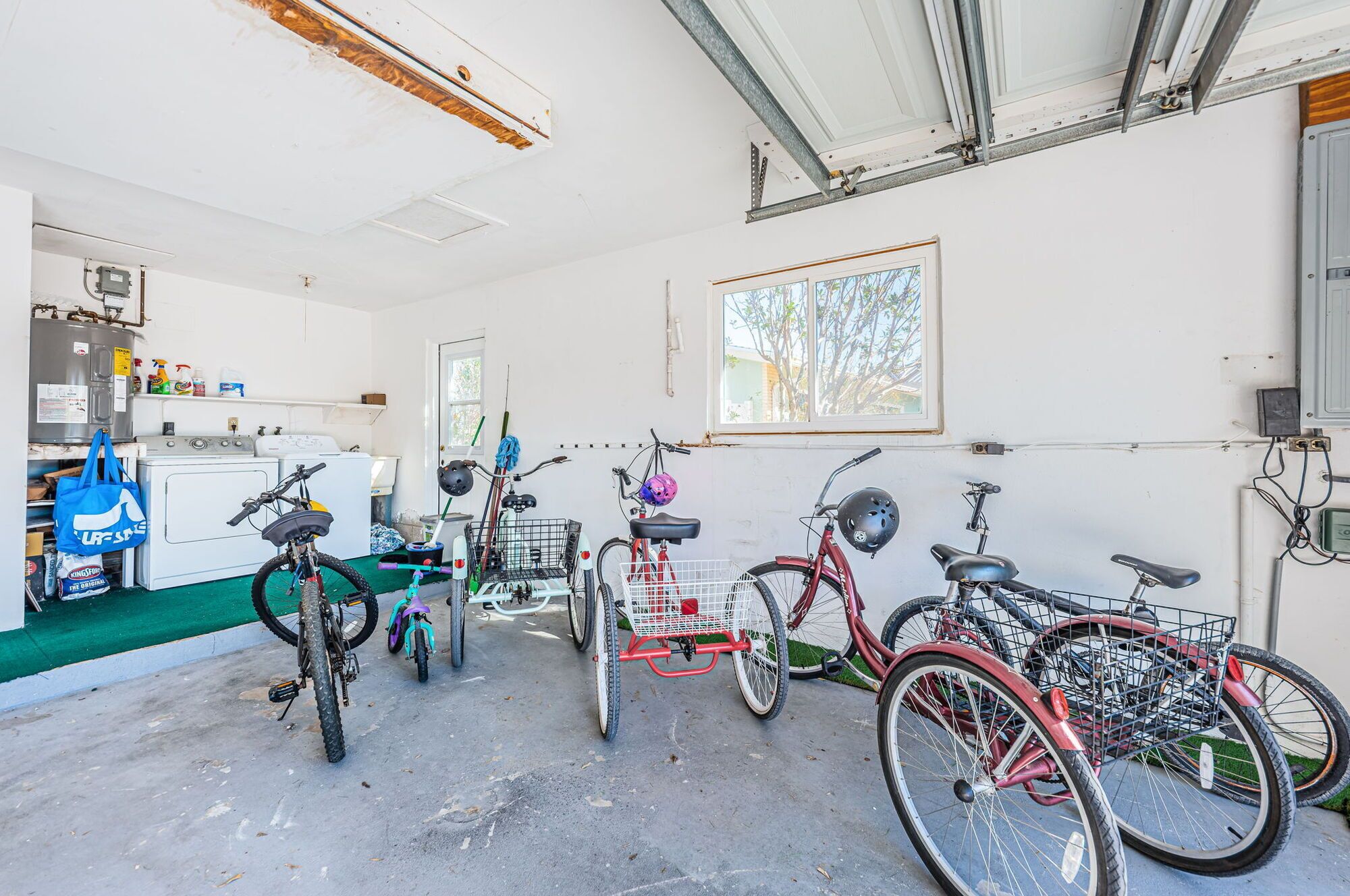 A garage with bicycles, a washing machine, and a window with a view of trees.