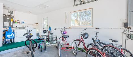 A garage with bicycles, a washing machine, and a window with a view of trees.