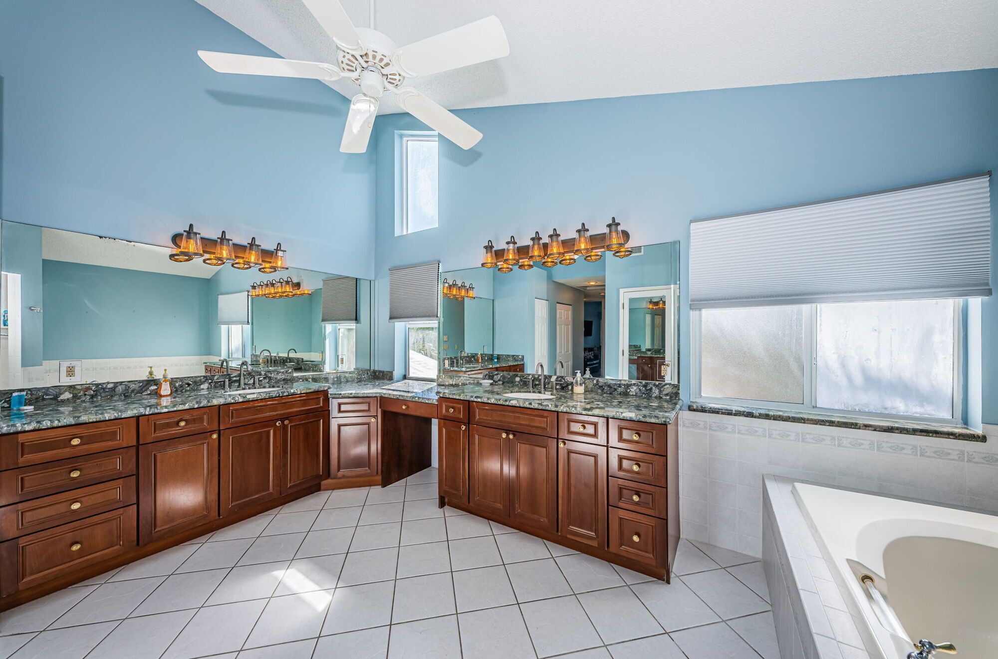 A spacious bathroom with a large vanity, a bathtub, and a ceiling fan.