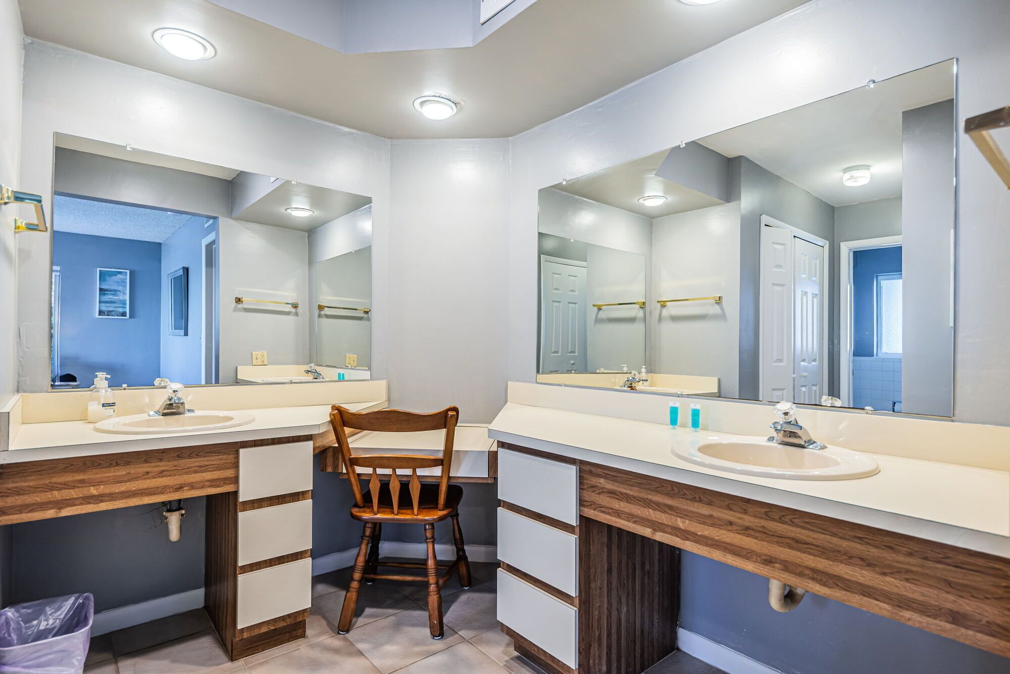 Une salle de bain avec deux lavabos, des meubles en bois et une chaise.