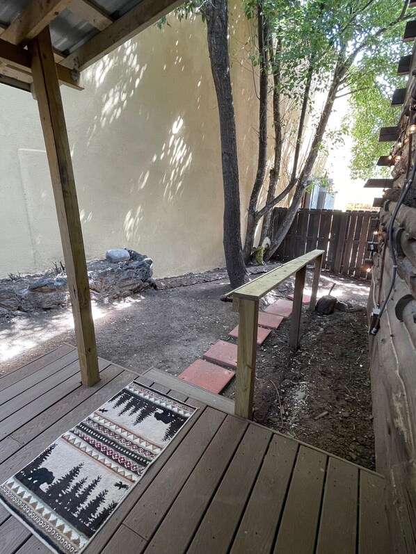 A wooden deck with a patterned rug, a bench, and a stone wall in the background. - Walk to Midtown, King Bed, Cozy Cabin! (Ruidoso)