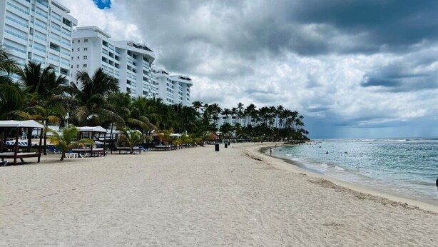 A beach with palm trees and a hotel in the background.