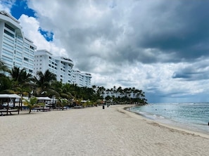 A beach with palm trees and a hotel in the background.
