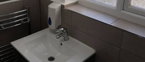 Un baño con lavamanos blanco, un espejo, una ventana con vidrio esmerilado y un inodoro.