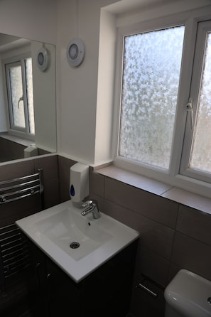 Ein Badezimmer mit weißem Waschbecken, einem Spiegel, einem Fenster mit Milchglas und einer Toilette.