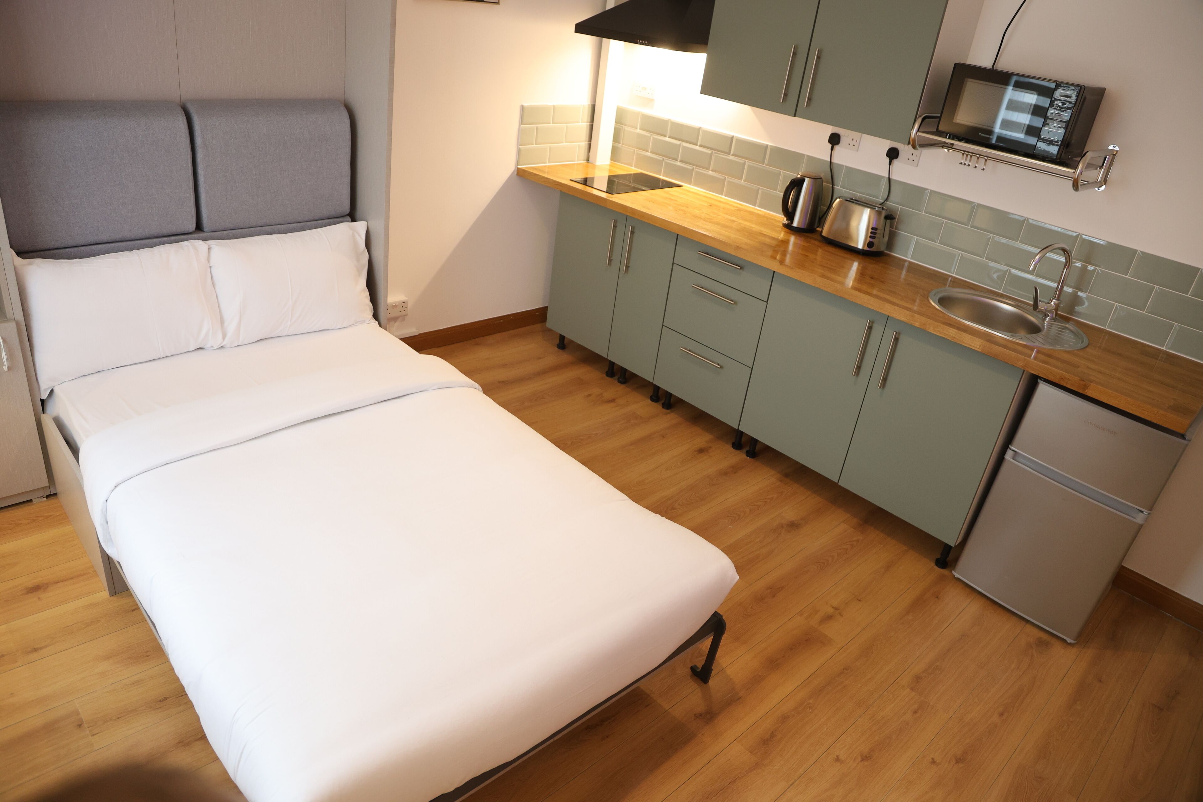 A bedroom with a bed, a kitchenette with a microwave, toaster, and sink, and a small refrigerator.