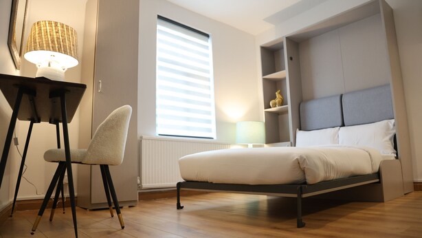 A modern bedroom with a bed, a desk with a lamp, and a chair. - Urban Hideaway Studio (London)