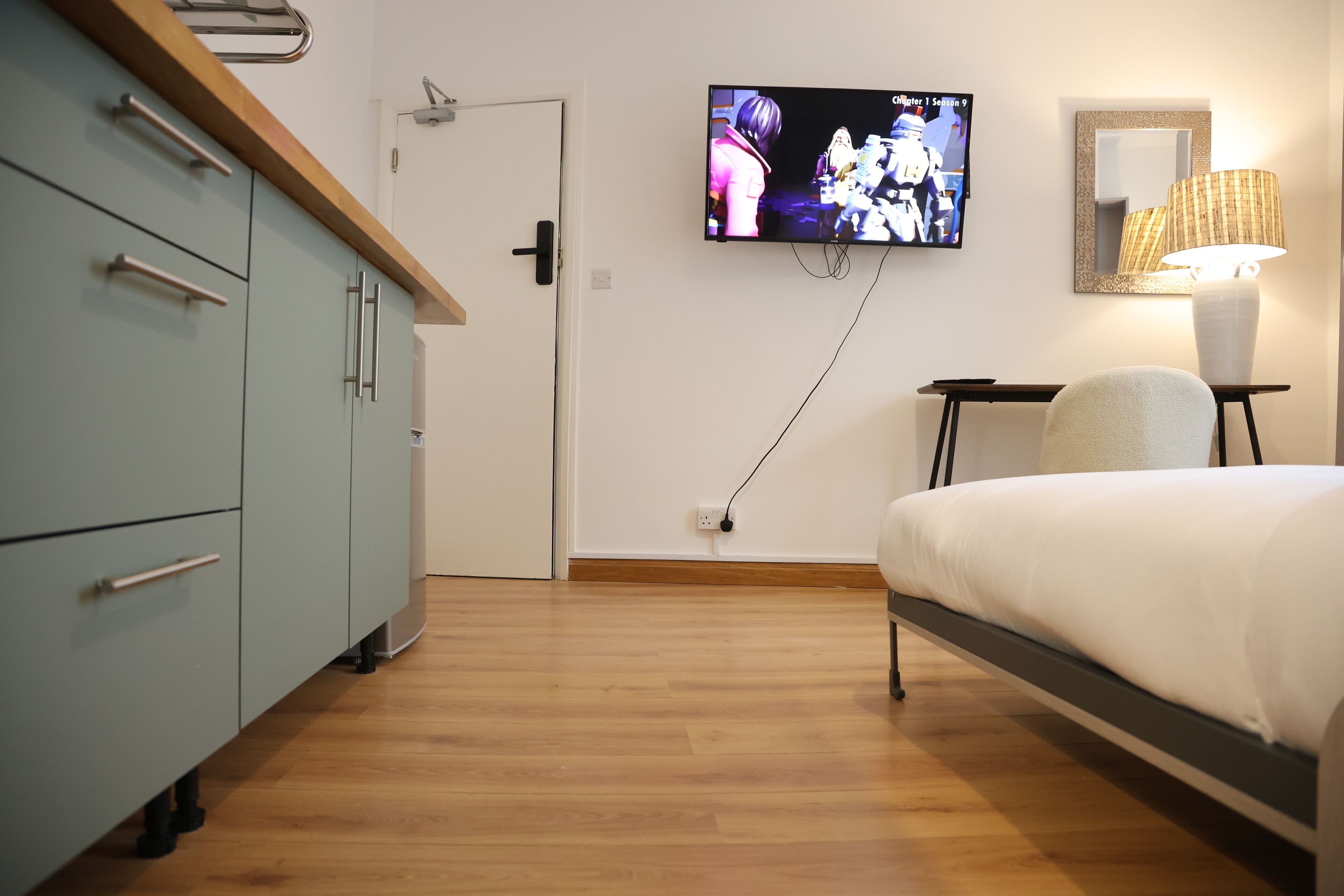 A bedroom with a bed, a TV mounted on the wall, a bedside table with a lamp, and a wardrobe.