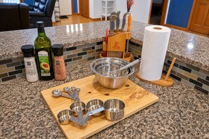 A kitchen counter with a cutting board, measuring cups, a mixing bowl, a bottle of olive oil, salt, and pepper. - Serene Rustic Retreat with Lake (Cuddebackville)