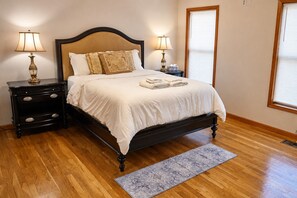 A neatly made bed with white linens, two bedside tables with lamps, and a wooden floor. - Serene Rustic Retreat with Lake (Cuddebackville)
