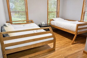 A room with two wooden bunk beds, a small bedside table, and a window with a view of greenery. - Serene Rustic Retreat with Lake (Cuddebackville)