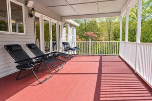 A covered porch with four lounge chairs, a white railing, and a red floor. - Serene Rustic Retreat with Lake (Cuddebackville)