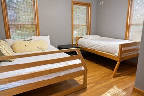 Una habitación con dos literas de madera, una mesita negra y una ventana con persianas.